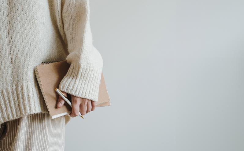 Personne vêtue d’un pull beige tenant un carnet