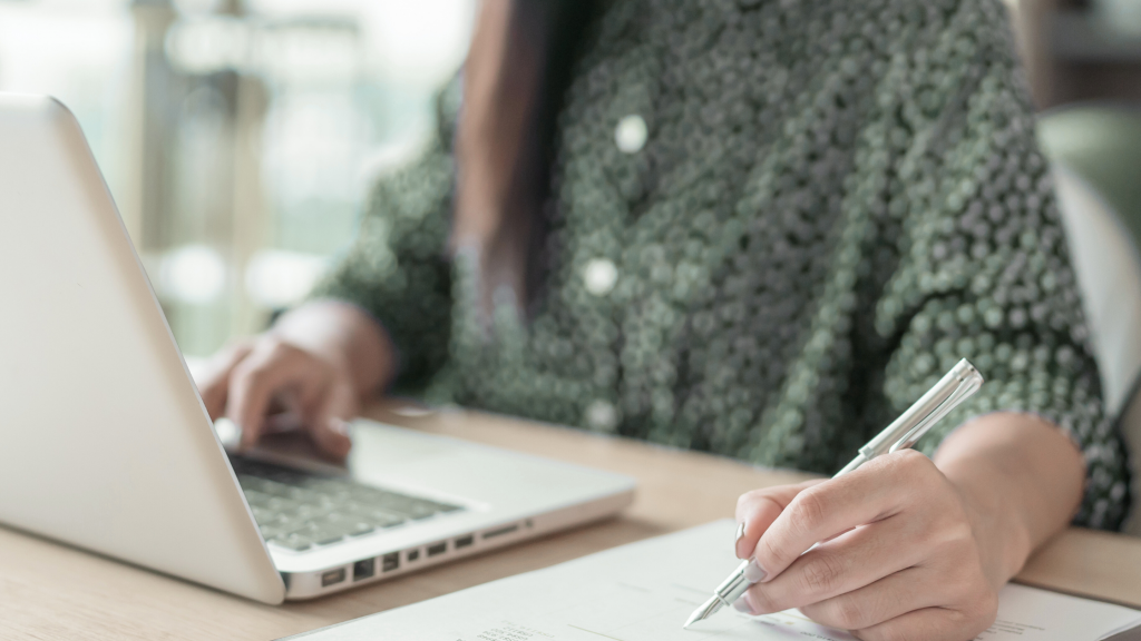 femme devant son ordinateur qui écrit sur un papier